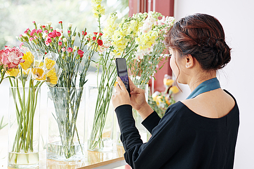 Young female florist photographing and posting fresh flowers in her store account to attract customer via social media