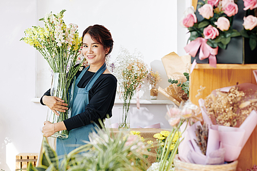 Happy young flower shop owner removing big vase with fresh flowers