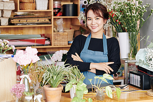 Portrait of young beautiful flowers shop owner standing at counter with arms folded