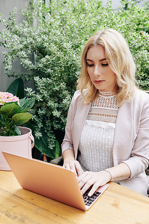 Pretty young woman sitting at table in her garden or backyard and working on laptop