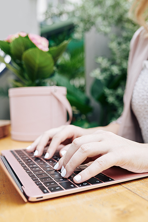 Hands of female freelancer typing on laptop when sitting at desk outdoors