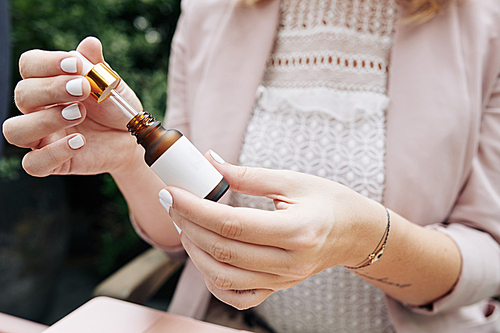 Hands of female entrepreneur opening bottle of natural essence for face skin and testing product