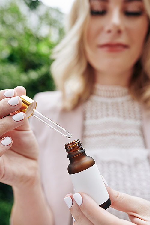 Organic cosmetics brand owner opening essence bottle with pipette when testing new product