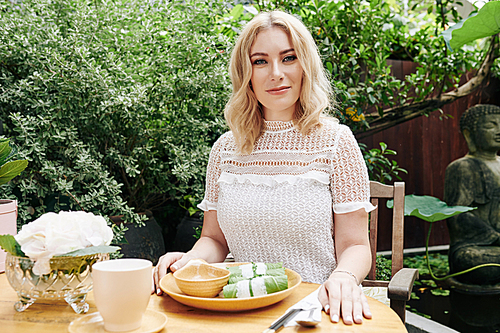 Beautiful smiling blond woman sitting at table in her backyard and eating tasty Asian food