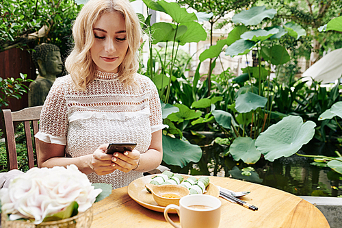 Smiling elegant woman eating tasty lunch and texting friends or business partners