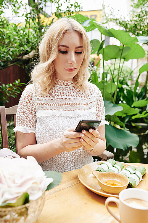 Serious young woman eating Asian food for business lunch and checking messages on her social media