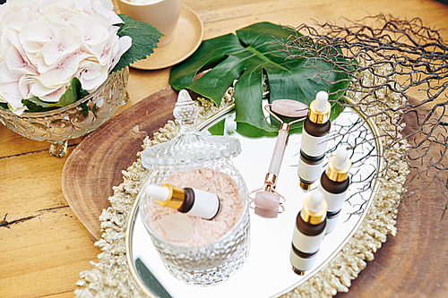 Small bottles with essence and emulsion and quartz face roller on metal tray in beauty salon