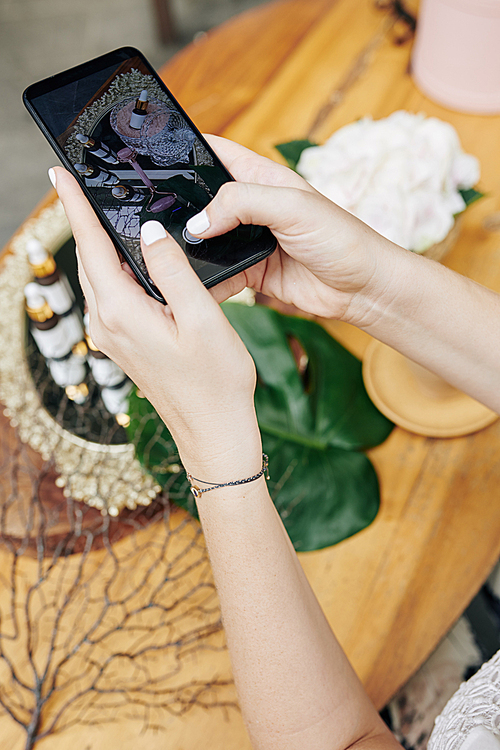 Hands of marketing manager photographing bottles with organic oils and essences for brand account on social media