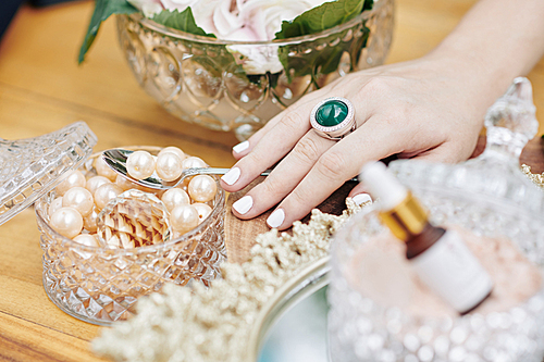 Hand of woman taking spoon of big pearls from crystal jewerly box