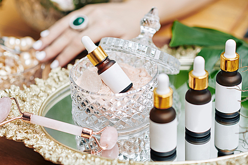 Bottles with oils and essences and quartz massage roller on tray on vanity of woman