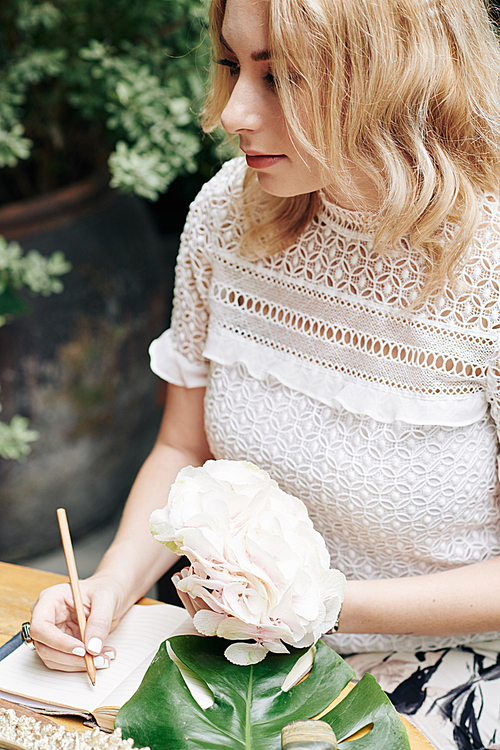 Pensive young woman with beautiful flower in hand filling her gratitude journal