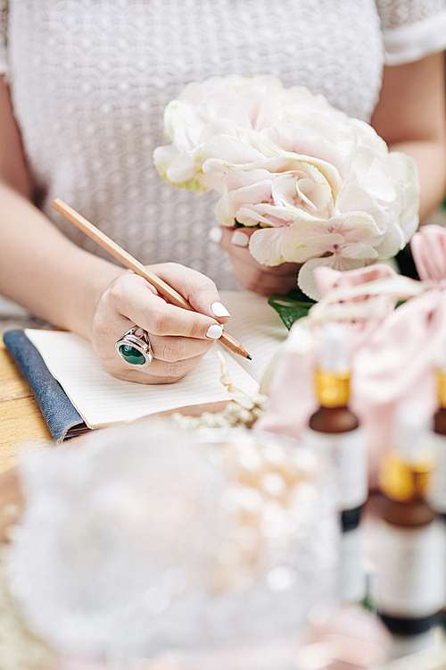 Close-up image of woman with flower in hand writing down ideas for new beauty treatments for her cosmetics brand