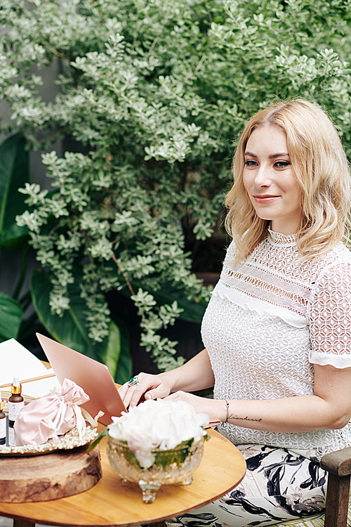 Beautiful successful young Caucasian business lady sitting at outdoor cafe and working on laptop