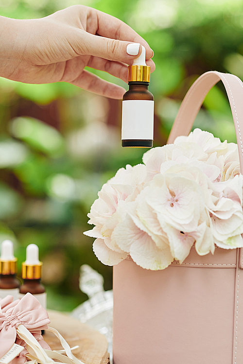 Female hand taking glass pipette dropper bottle with empty white sticker fromt the backet of flowers