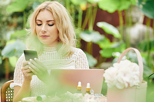 Beautiful young elegant business lady sitting outdoors and reading text messages in her smartphone