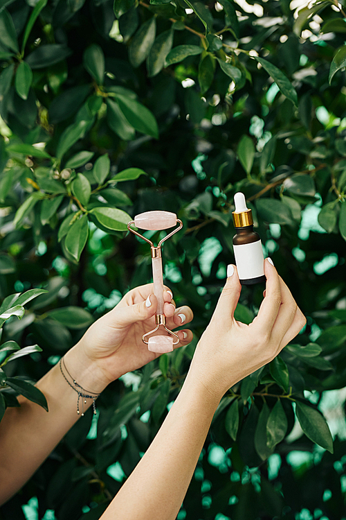 Small bottle of rejuvenating essence and quartz massage roller in hands of cosmetologist