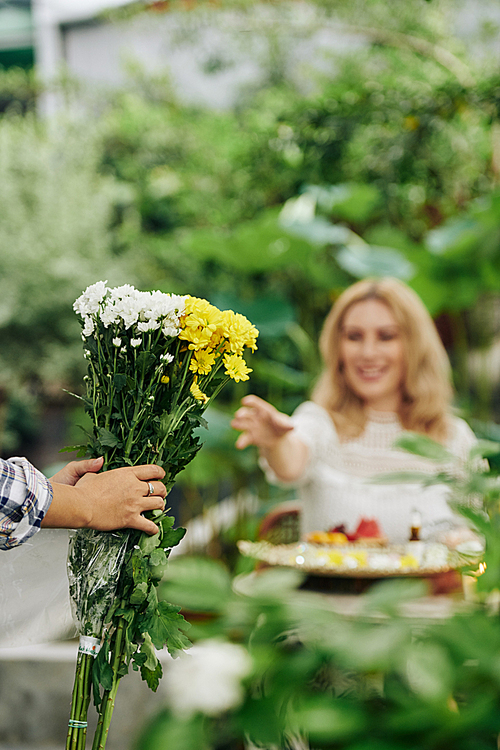 Gardener bringing bouquet of flowers to young smiling woman stretching arms towards it