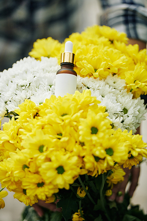 Small glass bottle of essential oil on bouquet of white and yellow flowers