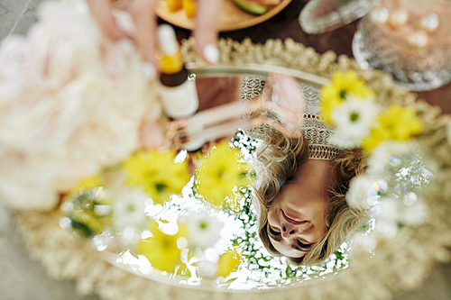 Reflection of young smiling woman in tray with beauty products and flowers