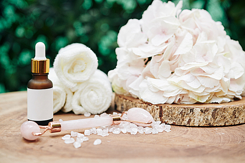 Light pink hydrangea flower, quartz massage roll and rejuvenating essence on wood stump