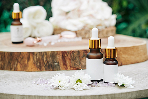 Small bottles with serums and essences on wooden table with flower petals and gemstones