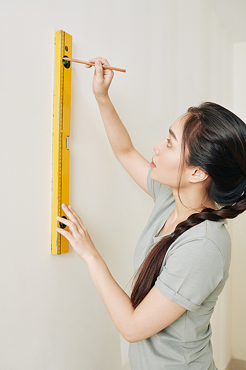 Pretty young Asian woman using spirit level for drawing horizontal line on the wall in her new house