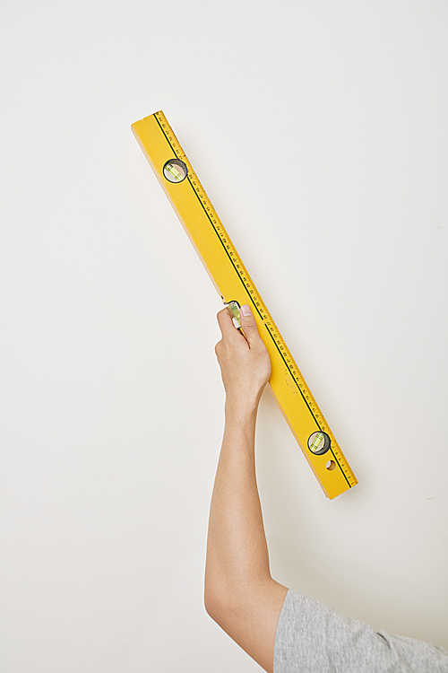 Hand of repairman holding spirit level against white wall in new apartment