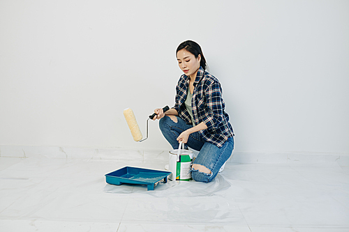 Beautiful young Asian woman pouring white paint in plastic tray and applying it with roller