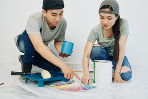 Young Asian couple in jeans and t-shirts choosing color for painting walls in their new apartment