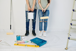 Couple holding can of paint and roller when standing at wall in new house they are going to paint