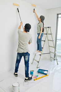 Short young woman standing on ladder when painting room walls with her boyfriend