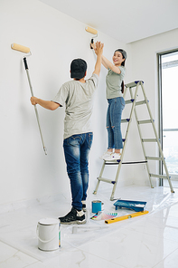 Cheerful young Asian boyfriend and girlfriend giving each other high five after finishing painting walls in bedroom