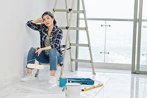 Exhausted young Vietnamese woman almost crying when having short break after painting walls in apartment