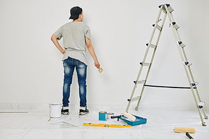 College student with brush painting wall in rented room in white color