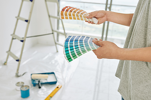 Paper palletes of paint swatches in hands of person choosing color for walls in new apartment