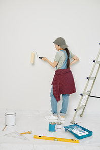 Pretty young Asian woman enjoying painting walls in her new apartment with roller