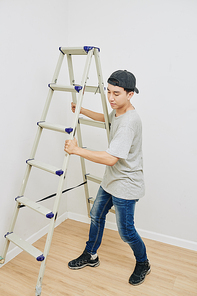 Young Asian man briging ladder to wall before painting it white