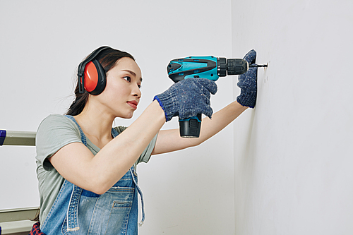 Pretty young Vietnamese woman concentrated on drilling wall in her room