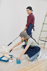 Young Asian couple with foam rollers painting walls in bedroom in white color