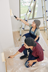 Young Vietnamese couple with foam rollers painting walls in in bedroom in their new house