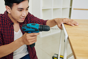 Positive excited handsome young Asian man using screwdriver for fixing table surface in place