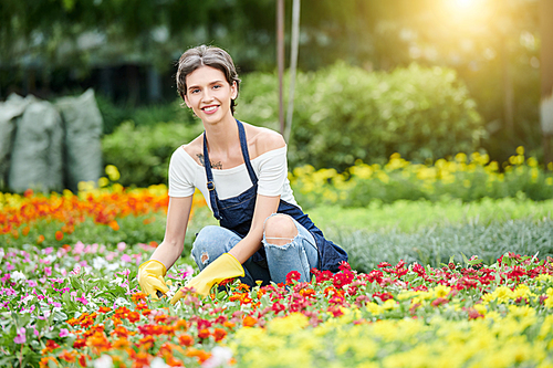 Cheerful pretty woman wearing protective clothes and gloves when working with plans and flowers in her garden