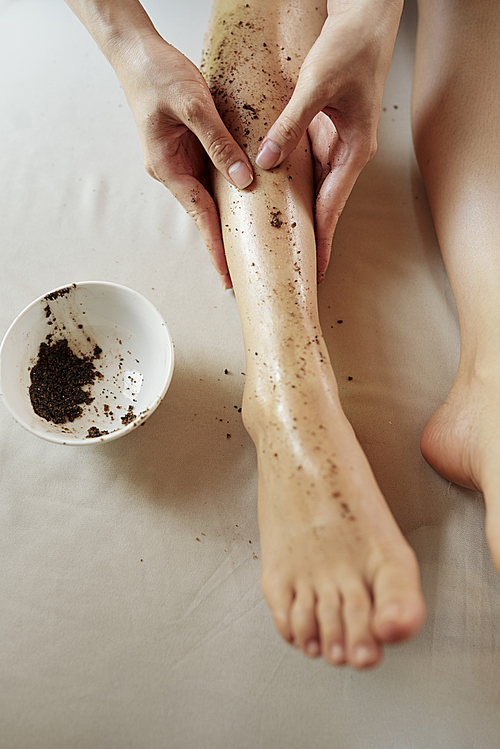 Young woman scrubbing her legs with natural coffee scrub after taking bath, view from above