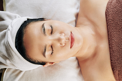 Young beautiful Vietnamese woman resting with eyes closed after refreshing skin treatment, view from above