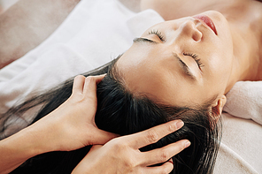 Close-up image of beautician massaging head of female client relaxing on massage bed