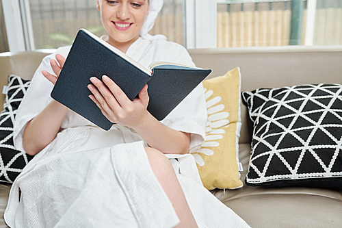 Relaxed smiling young woman reading a book after taking bath at home