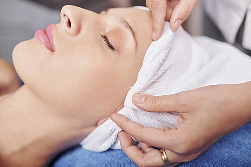 Bautician covering hair of female client with towel before beauty procedure