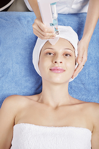 Cheerful young woman smiling and enjoying carbone face peeling in beauty salon, view from above