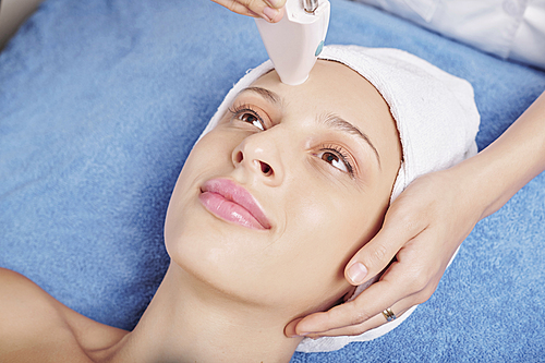 Young positive Caucasian woman having laser facial treatment in spa salon