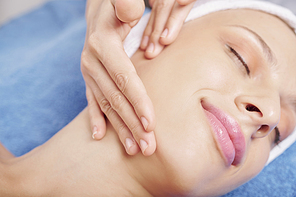 Close-up image of beautician massaging face of pretty young Caucasian woman